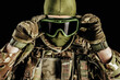 Photo of soldier in level 3 armored vest ammunition, tactical gloves putting on tactical goggles on black background.