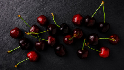 Wall Mural - ripe cherries on black background top view. Pattern of fresh red  cherries with sprig . Cherry berries laid on black background. Creative layout. Food concept