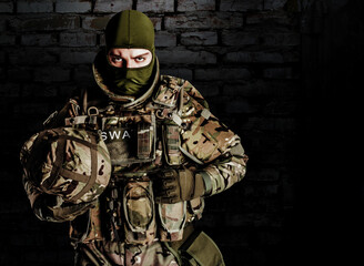 Wall Mural - Photo of fully equipped swat soldier in heavy level 3 amor ammunition and rifle standing on dark bricks background.