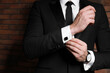Man wearing stylish suit and cufflinks near brick wall, closeup