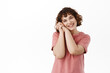 © Cookie Studio - Tender and beautiful curly girl, smiling happy, admire at something romantic and cute, leaning head on hands and gazing lovely, standing in t-shirt against white background