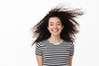 Beauty. Brunette woman close eyes and smile happy, wind blowing at her face as curly hair strands flying in air, standing in t-shirt against white background