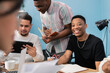 © ABCreative - A group of students sit in a classroom at a table with books, notes, and a computer and work on a project for college. They are reviewing ideas on the tablet, jotting down notes, discussing