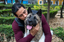 Young Hispanic Man Petting And Holding His American Akita Dog In The Park