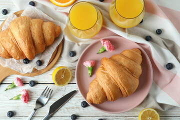 Concept of tasty breakfast with croissants on white wooden background