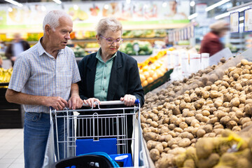 mature spouses chooses potato in vegetable section of supermarket