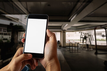 A man hand holding smart phone device in the fitness room view background