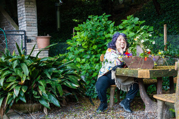 Sticker - Senior blue-haired female sitting in the garden with beautiful flowers in a wooden pot