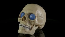 Skull With Blue Eyes. A Human Skull With Blue Eyes On The Black Background.