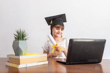 Wall Mural - little girl with graduation cap and diploma with laptop on white background. graduation concept.