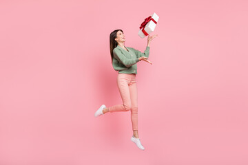 Poster - Full size profile photo of optimistic cool girl jump with gift up wear sweater trousers sneakers isolated on pink color background