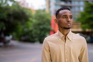 Wall Mural - Portrait of handsome black young African businessman thinking outdoors in city