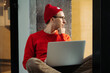 © Yury - Millennial freelancer web designer, writer, journalist man work remotely on laptop sit pensive on windowsill. Hipster guy look in window with hand under chin think on new project idea development plan