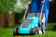 Close-up of a man in overalls with a lawn mower cutting green grass in a modern garden. Lawn mowing machine.