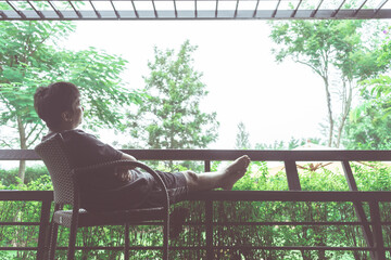 Young is sitting alone on the bench looking at forest in evening. A lonely young man sitting on a bench in a park.Elderly gentleman on park bench in contemplation