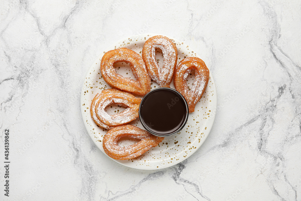 Plate with tasty churros and melted chocolate sauce on light background