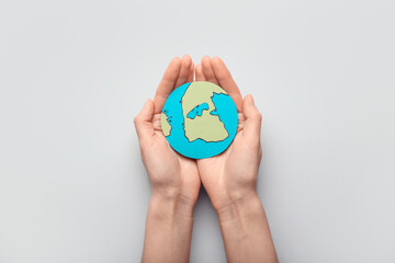 Human hands with paper planet Earth on light background