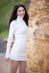 Poster - Young fashion woman with long hair in white dress relax near beautiful stones. Happy beach lifestyle