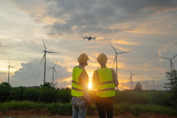 Teamwork of Asian windmill engineer group, worker working, control a drone on site at wind turbines field or farm, clean energy source. Eco technology for electric. industry nature environment. People