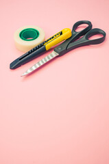 Poster - Closeup shot of scissors adhesive tape and a utility knife on a pink background