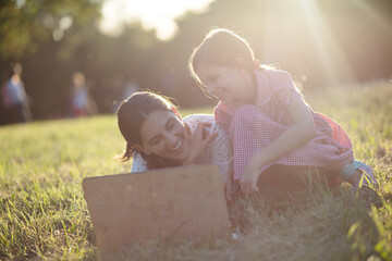 Wall Mural -   Mother and daughter sitting on grass and using laptop.