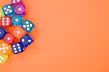 Top View Of Colorful Plastic Dice Against An Orange Background With Space For Text