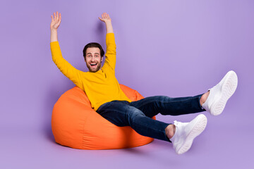 Sticker - Portrait of attractive funky cheerful man sitting in bag chair having fun celebrating isolated over pastel violet purple color background