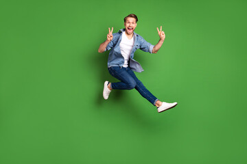 Sticker - Full length body size photo of young guy jumping happy showing v-sign gesture isolated vivid green color background