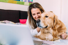 Young Woman With Dog On Bed Looking At Laptop