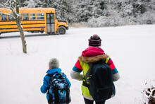 Rear View Of Children Walking Towards School Bus In Snow