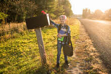 Boy Standing At Mailbox On Roadside At Sunset