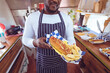 © Wavebreak Media - Midsection of african american man in food truck holding hotdog and chips