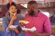 © Wavebreak Media - Smiling diverse couple eating hot dog and potato wedges by food truck on sunny day