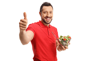 Wall Mural - Smiling young man in a red t-shirt eating a healthy fresh salad and showing thumbs up