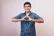 © alex fernandezch - Hombre joven y feliz hace gestos de amor con sus manos. Modelo aislado en fondo blanco con camisa azul