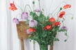 Beautiful red and purple poppies bouquet on wooden chair on background of rustic textile in room. Gathering countryside wildflowers. Common poppy and Opium poppy flowers in vase