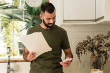 Man With Partial Hand Amputation Holding Papers And Mobile Phone At Kitchen.