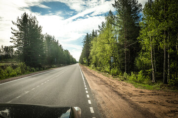 Wall Mural - The road among the Karelian taiga. Pine forest on the side of the road. Trip to Karelia. Highway among the trees. Driving on a trip to beautiful places. Karelia. Day.