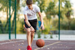 © Natali - A cute boy in a white t-shirt plays basketball on a city playground. Active teen enjoying an outdoor game with an orange ball. Hobby, active lifestyle, sport for kids.