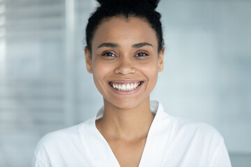 Portrait of happy beautiful African girl wearing bathrobe, smiling at camera, showing white perfect healthy teeth. Morning bath procedures, dental care, home spa, hygiene concept. Head shot