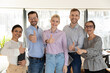 © fizkes - Portrait of successful diverse employees team showing thumbs up, standing in office room, happy confident businesspeople interns workers looking at camera, human resources and employment concept