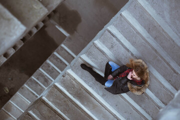 Canvas Print - Top view of a young female in a coat and long boots posing sitting on the stairs