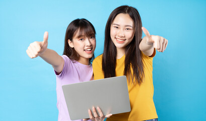 Two beautiful young asian girls using laptop on blue background