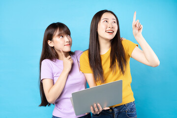 Two beautiful young asian girls using laptop on blue background