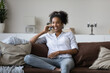 © fizkes - Happy african american woman relaxing on comfortable sofa, holding pleasant distant conversation in smartphone, discussing life events with friends, chatting with family remotely, listening good news.