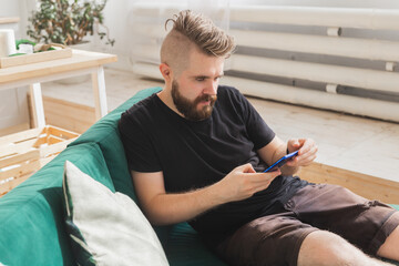 Relaxed man using a smartphone sitting on green couch in the living room at home