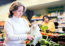 Closeup Portrait Of Elderly Woman Putting Fresh Green Beans In Plastic Bag While Shopping In Vegetable Section Of Supermarket