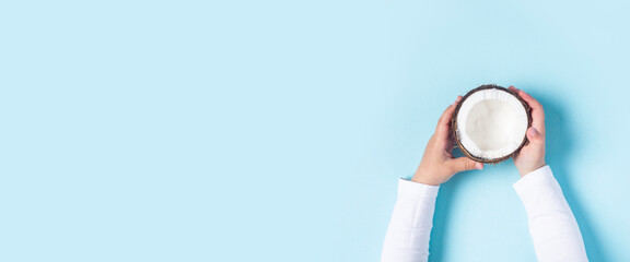 Wall Mural - children's hands are holding half a coconut on a blue background. Top view, flat lay. Banner