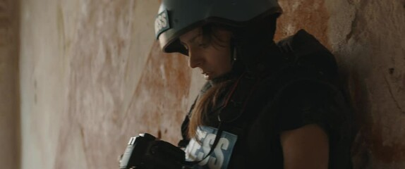 Wall Mural - Caucasian female war journalist wearing protective helmet and bulletproof vest gear taking photos during military operation. Shot with 2x anamorphic lens