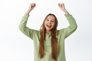 Wall Mural - Cheerful girl rejoicing, winning and shouting with joy yes, raising hands up, rooting for team, become winner, achieve goal and celebrating, standing over white background